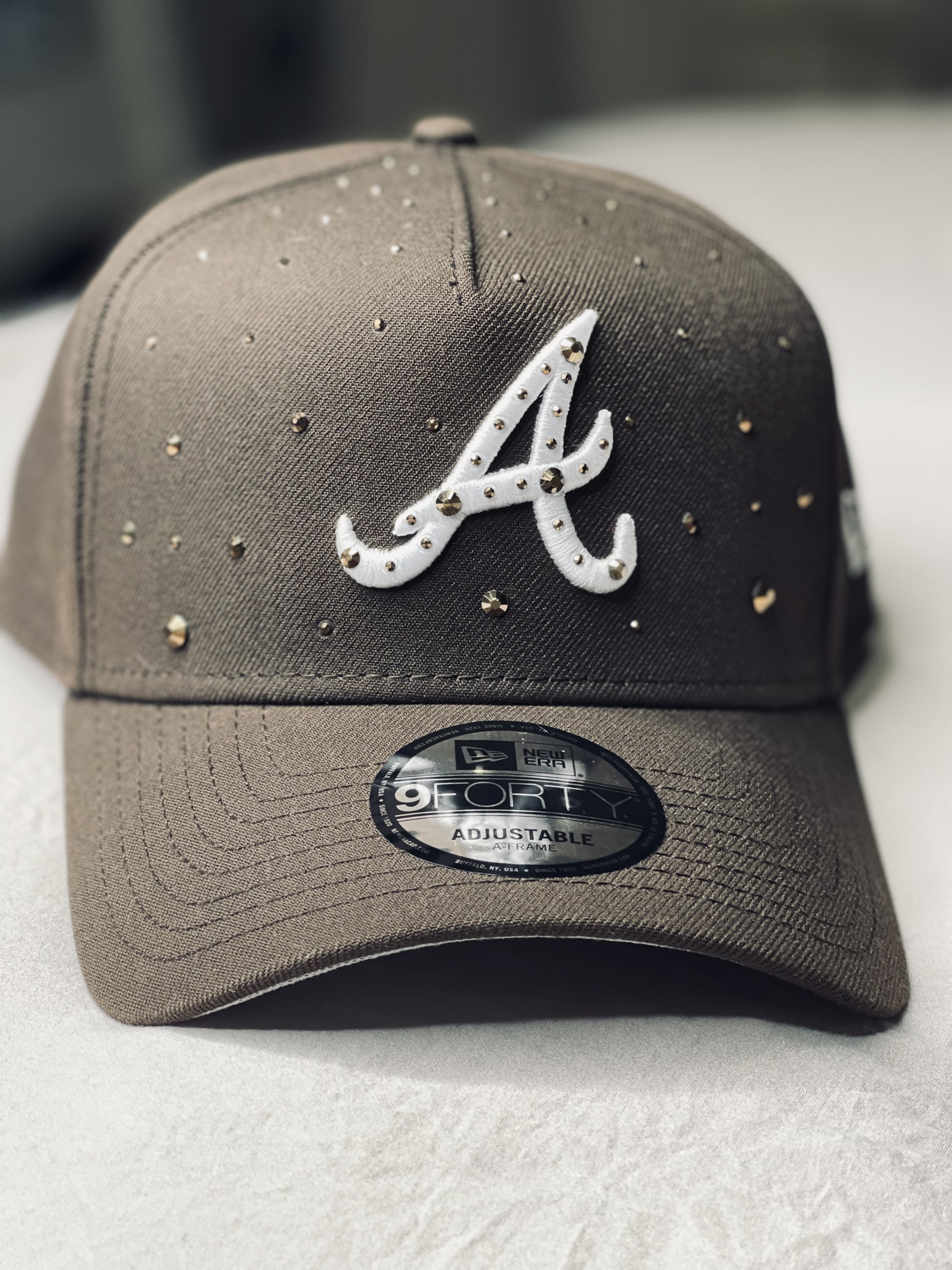 Sand-colored cap with crystal monogram and scattered studs.