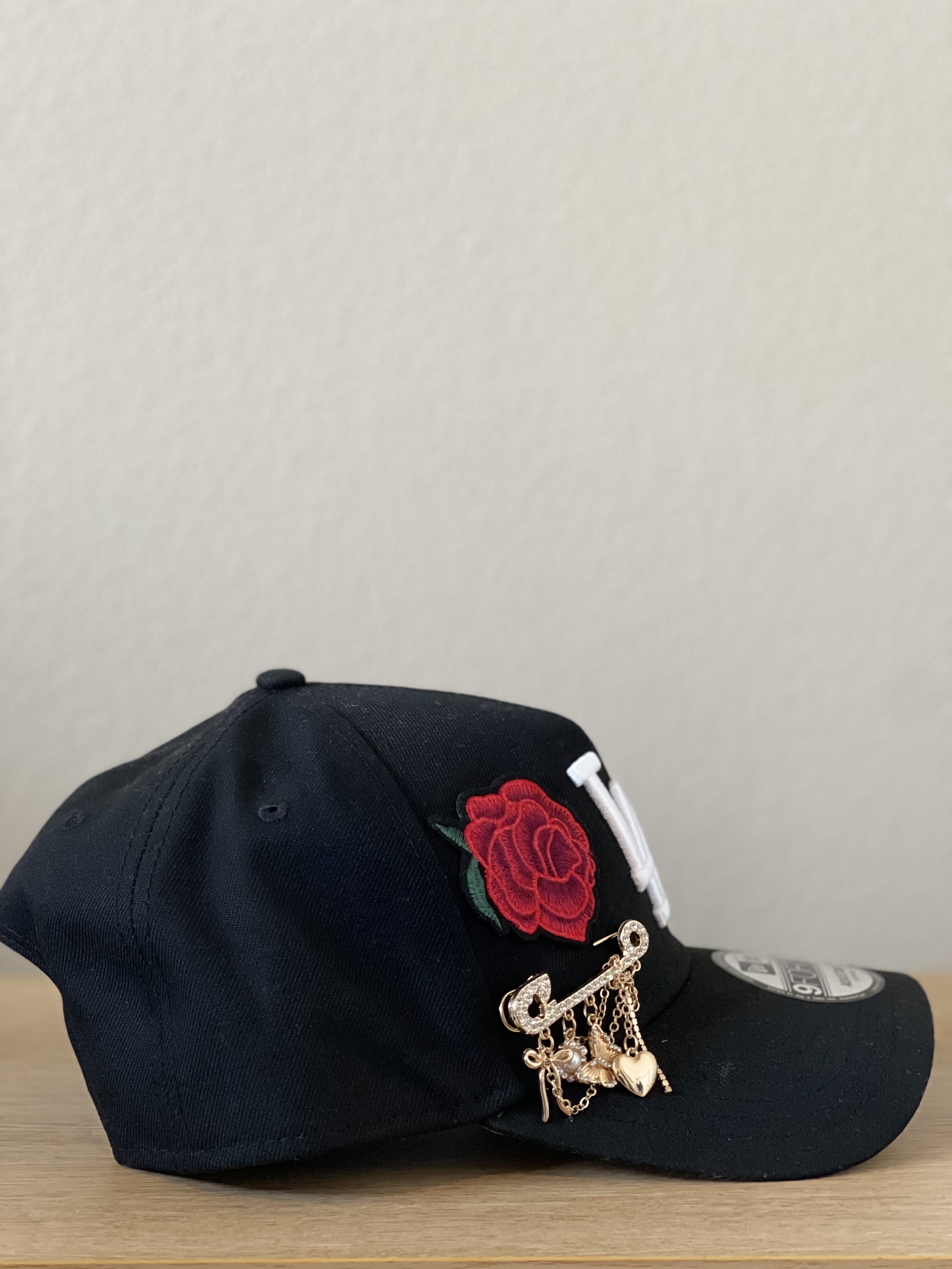 Black LA snapback with rose applique and layered gold charms, front view.